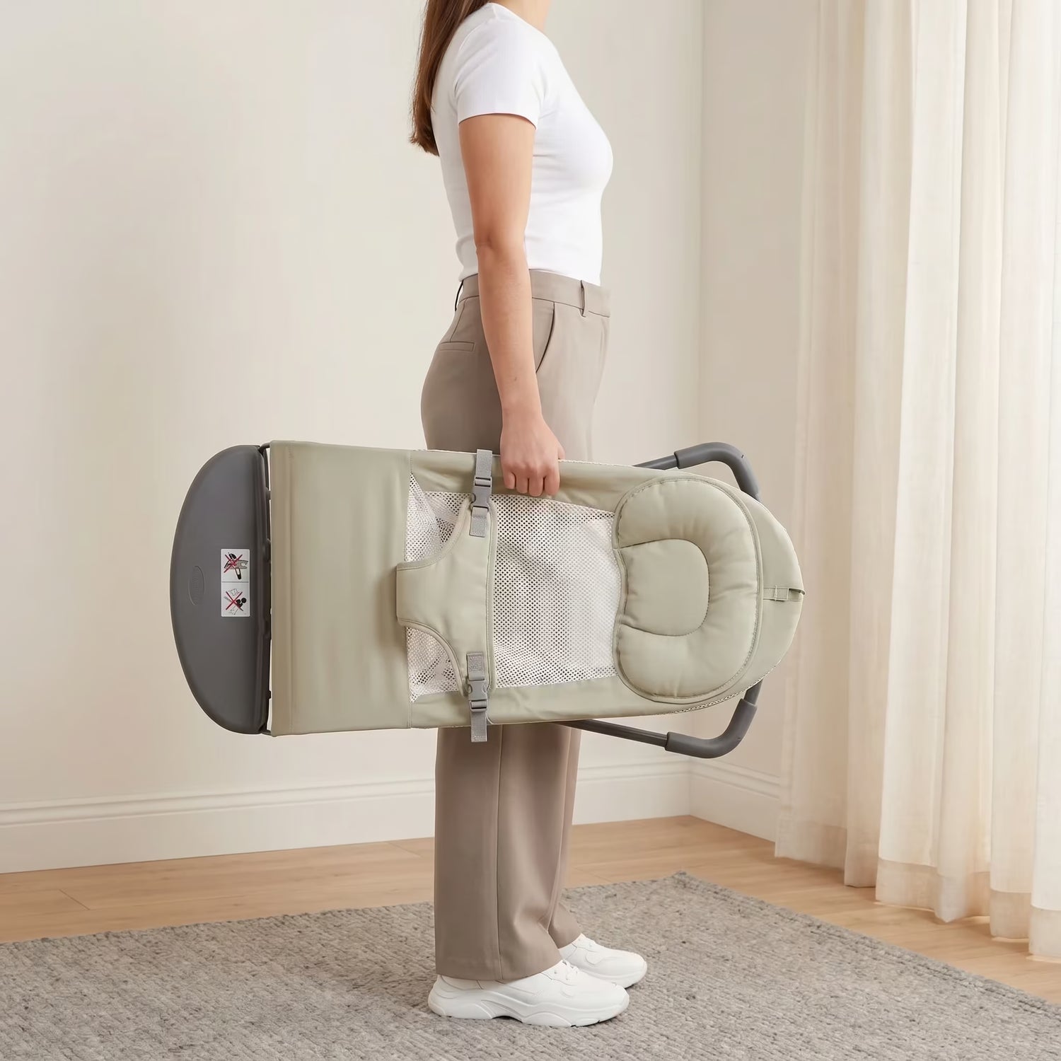 Person holding a folded baby carrier in a room with light-colored walls and curtains.