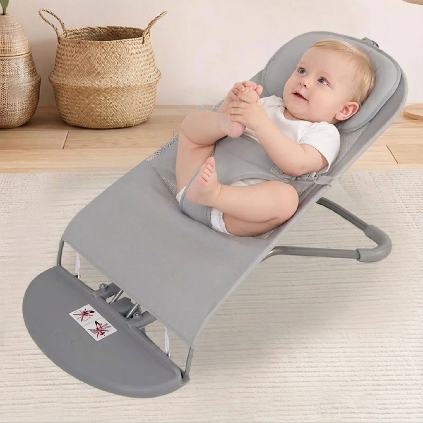 Baby in a gray baby bouncer on a light wooden floor with woven baskets in the background.