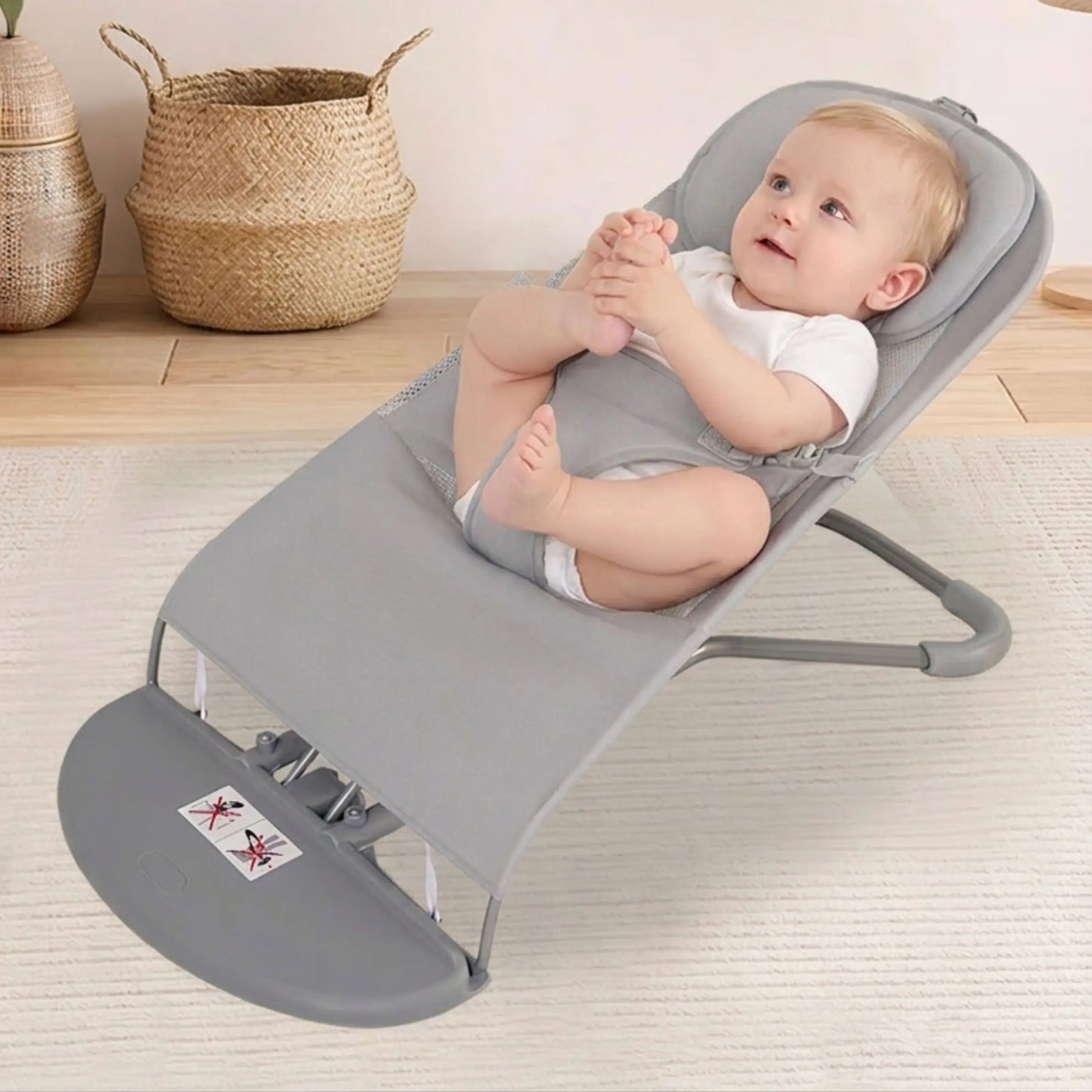Baby in a gray baby bouncer on a light wooden floor with woven baskets in the background.