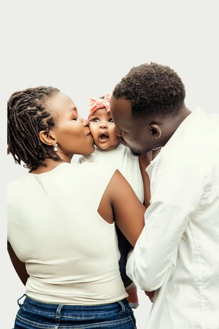 Two adults kissing a baby on a white background