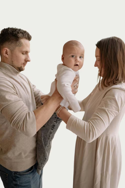 Man and woman holding a baby against a plain background