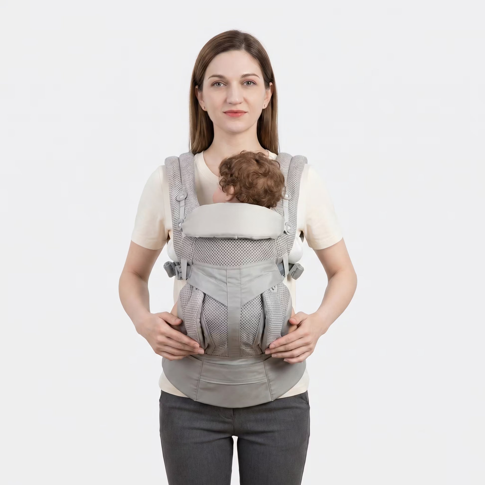 Woman wearing a baby in a gray baby carrier against a white background